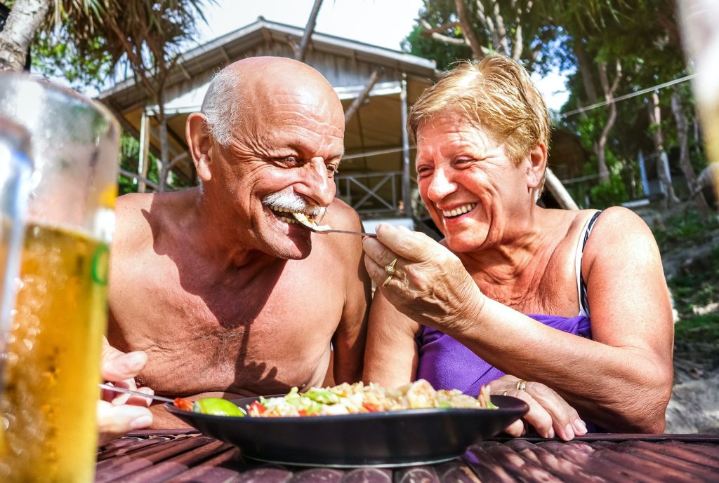 Retired couple having fun eating local food at thai restaurant beach bar outdoors